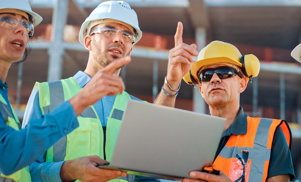 Construction engineers with a laptop in hand look at the project and discuss it